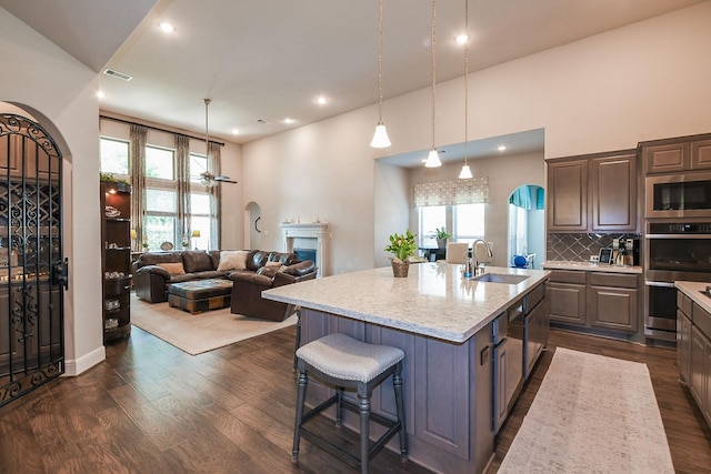 13326 Hartford Bay Trl, Cypress, TX 77429 - kitchen featuring appliances with stainless steel finishes, arched walkways, dark wood-type flooring, a center island with sink, and a kitchen breakfast bar