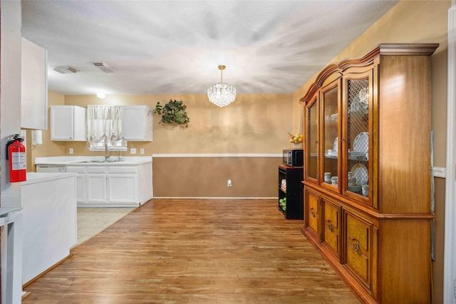 8202 Caddo Rd, Houston, TX 77078 - kitchen featuring light wood-type flooring, white cabinetry, a chandelier, glass insert cabinets, and light countertops