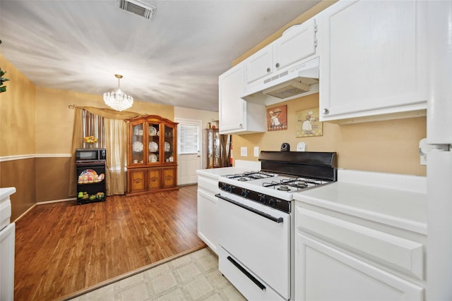 8202 Caddo Rd, Houston, TX 77078 - kitchen featuring white range with gas stovetop, black microwave, under cabinet range hood, a chandelier, and white cabinets