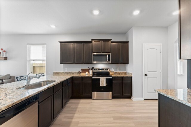 20730 Solstice Point Dr, Hockley, TX 77447 - kitchen with stainless steel appliances, a sink, dark brown cabinetry, light wood-style flooring, and light stone counters