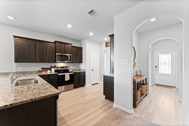 20730 Solstice Point Dr, Hockley, TX 77447 - kitchen with appliances with stainless steel finishes, a sink, arched walkways, dark brown cabinets, and light stone counters