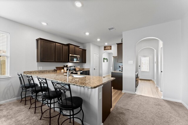 20730 Solstice Point Dr, Hockley, TX 77447 - kitchen with arched walkways, stainless steel microwave, dark brown cabinets, a breakfast bar, and light stone counters
