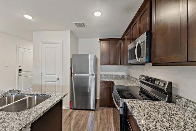 302 Connecticut St, Houston, TX 77029 - kitchen with appliances with stainless steel finishes, a sink, light wood finished floors, dark brown cabinetry, and light stone counters