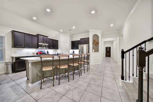 7411 Nottington Ct, Spring, TX 77379 - kitchen featuring stainless steel appliances, a breakfast bar area, light tile patterned flooring, an island with sink, and ornamental molding