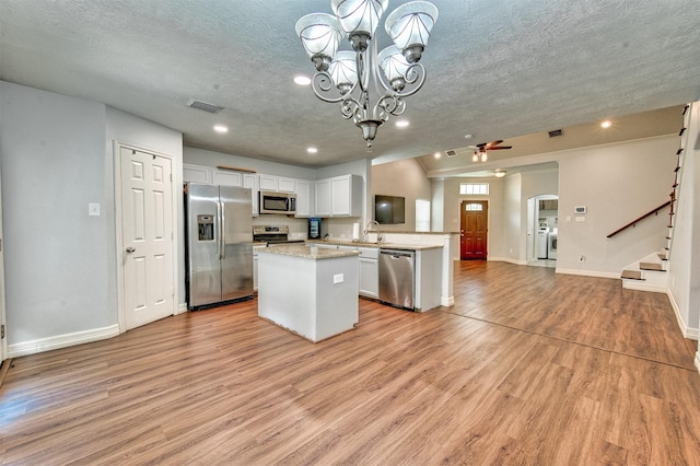 7022 Raven Cliffs Ln, Spring, TX 77379 - kitchen with stainless steel appliances, open floor plan, a textured ceiling, a kitchen island, and light wood-style floors