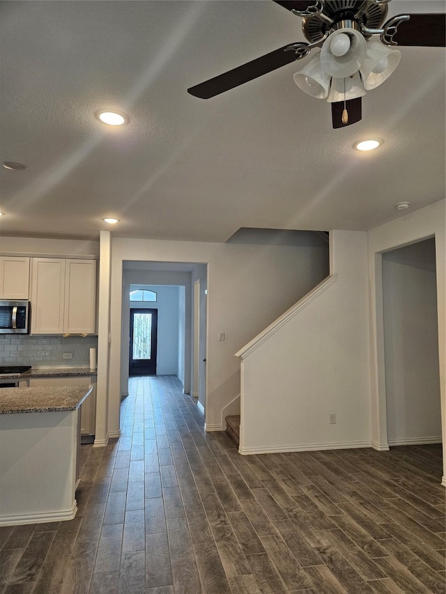 7927 Chukka Dr, Fulshear, TX 77441 - kitchen with stainless steel microwave, dark wood-style flooring, white cabinetry, decorative backsplash, and dark stone countertops