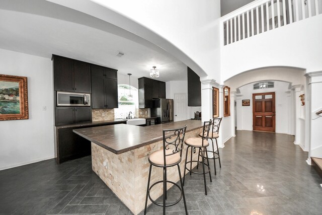 7410 Lassiter Hollow Ln, Richmond, TX 77407 - kitchen featuring stainless steel appliances, decorative columns, arched walkways, dark countertops, and a kitchen breakfast bar