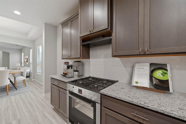 24708 Sonora Crescent Cir, Huffman, TX 77336 - kitchen with stainless steel range with gas stovetop, dark brown cabinets, baseboards, light stone counters, and light wood-type flooring