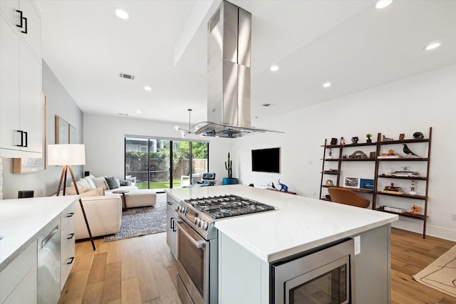 823 Aurora St, Houston, TX 77009 - kitchen with island exhaust hood, stainless steel appliances, open floor plan, light wood finished floors, and white cabinets