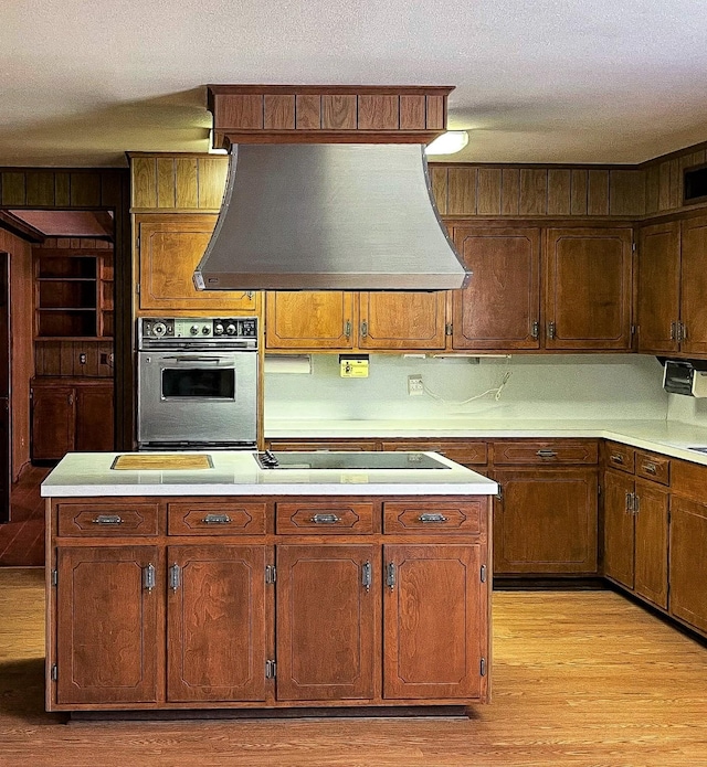 409 W Collier St, Jasper, TX 75951 - kitchen featuring oven, custom range hood, black electric cooktop, light wood-style floors, and light countertops
