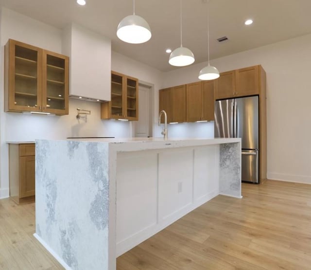 136 E 37th St, Houston, TX 77018 - kitchen featuring freestanding refrigerator, brown cabinetry, light wood-type flooring, an island with sink, and glass insert cabinets