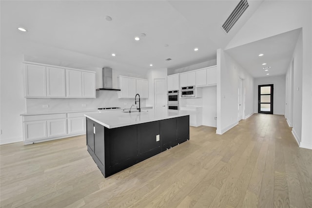 12211 Grey Plover Ct, Conroe, TX 77304 - kitchen with wall chimney range hood, white cabinetry, a spacious island, light countertops, and light wood finished floors