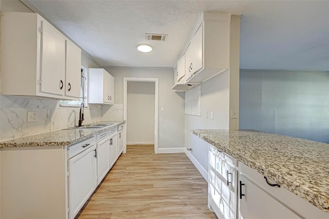 5102 Lyndhurst Dr, Houston, TX 77033 - kitchen with a sink, light wood-style flooring, tasteful backsplash, white cabinetry, and a textured ceiling