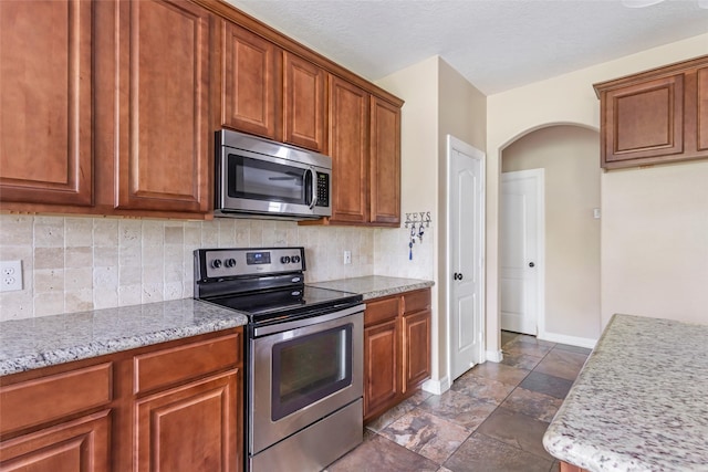 1511 Tournament Ct, Crosby, TX 77532 - kitchen with appliances with stainless steel finishes, arched walkways, backsplash, and brown cabinetry