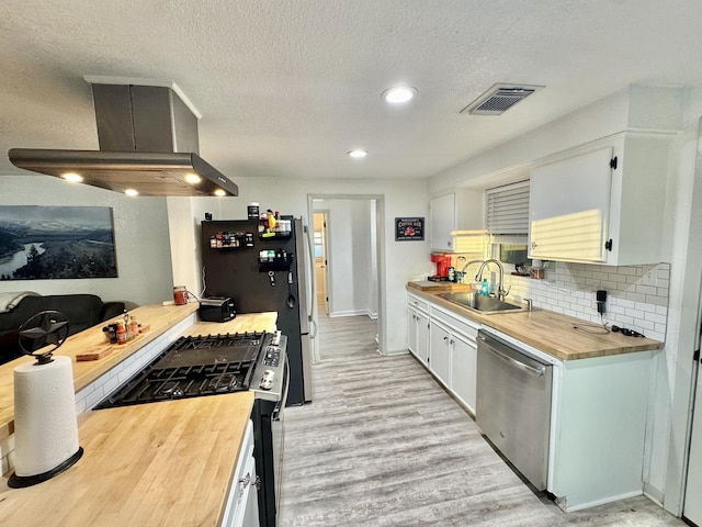 11837 13th St, Santa Fe, TX 77510 - kitchen featuring appliances with stainless steel finishes, butcher block counters, wall chimney exhaust hood, a sink, and light wood finished floors