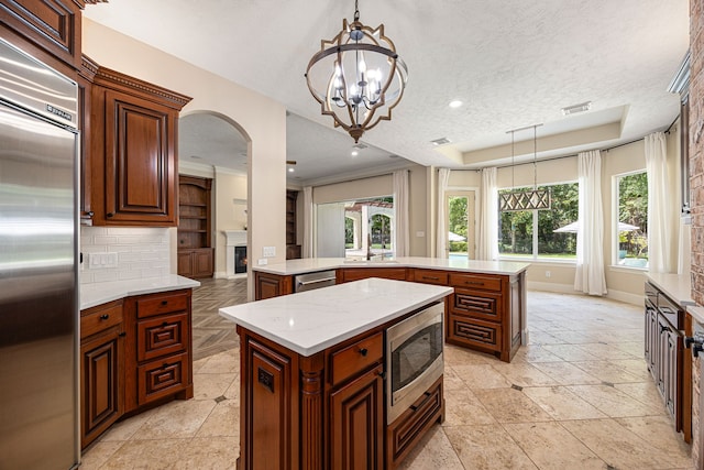 24914 Misty Heath Ln, Katy, TX 77494 - kitchen with built in appliances, a kitchen island, arched walkways, a lit fireplace, and baseboards