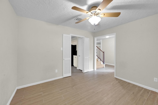 6606 Chancellor Dr, Spring, TX 77379 - empty room with light wood-style floors, baseboards, a ceiling fan, stairs, and a textured ceiling