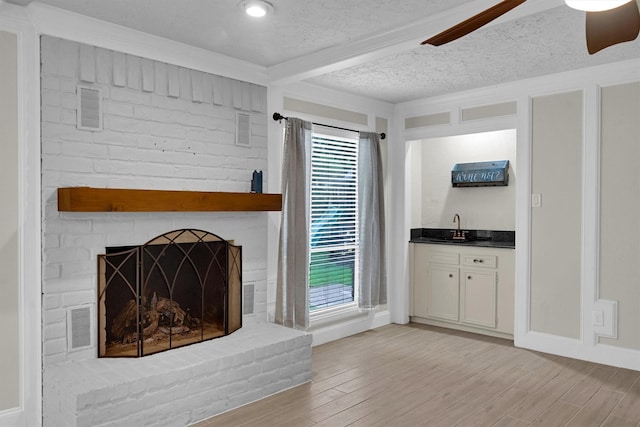 6606 Chancellor Dr, Spring, TX 77379 - unfurnished living room featuring wet bar, light wood-type flooring, a textured ceiling, a brick fireplace, and beamed ceiling