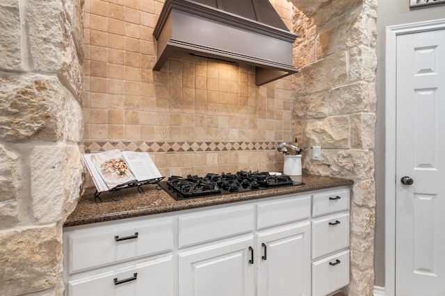 28622 Champions Dr, Magnolia, TX 77355 - kitchen featuring black gas stovetop, custom range hood, decorative backsplash, white cabinetry, and dark stone countertops