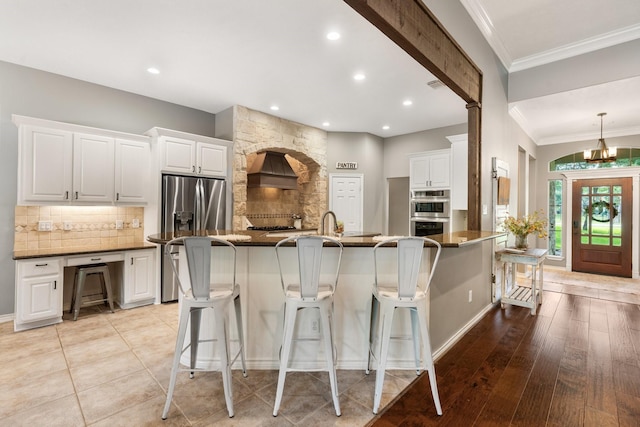 28622 Champions Dr, Magnolia, TX 77355 - kitchen with crown molding, backsplash, a kitchen breakfast bar, appliances with stainless steel finishes, and white cabinetry