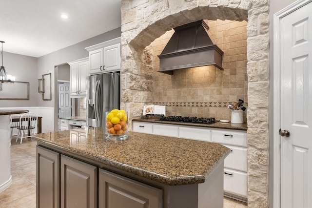 28622 Champions Dr, Magnolia, TX 77355 - kitchen with custom range hood, stainless steel fridge, black gas stovetop, backsplash, and a center island