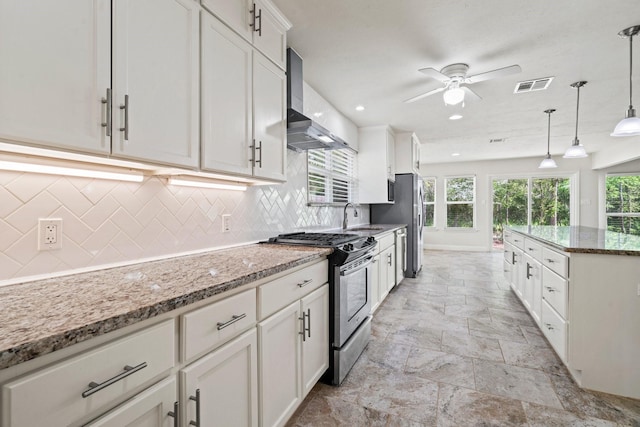 12006 Acorn Oak St, The Woodlands, TX 77380 - kitchen featuring stainless steel range with gas cooktop, wall chimney range hood, ceiling fan, stone tile flooring, and tasteful backsplash