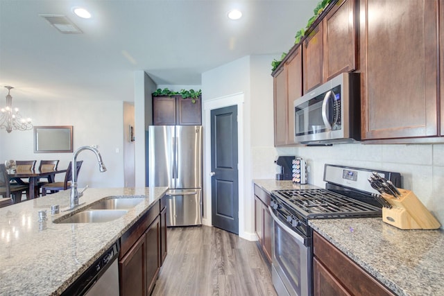 12413 S Hill Ct, Magnolia, TX 77354 - kitchen featuring appliances with stainless steel finishes, a sink, light wood finished floors, light stone counters, and decorative backsplash