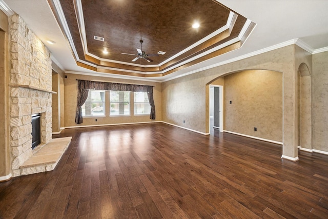 22611 Pineleigh Ct, Tomball, TX 77375 - unfurnished living room featuring a tray ceiling, ceiling fan, a stone fireplace, dark wood finished floors, and arched walkways