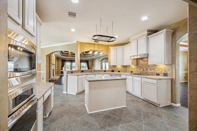 22611 Pineleigh Ct, Tomball, TX 77375 - kitchen with arched walkways, appliances with stainless steel finishes, a peninsula, white cabinets, and crown molding