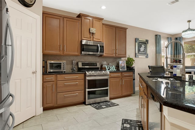 16946 Creek Mountain Dr, Houston, TX 77084 - kitchen with appliances with stainless steel finishes, brown cabinetry, dark stone countertops, decorative backsplash, and light tile patterned floors