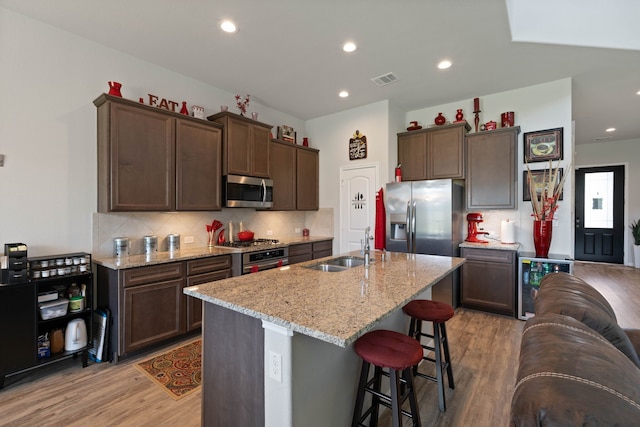25718 Balsamwood Dr, Tomball, TX 77375 - kitchen featuring appliances with stainless steel finishes, beverage cooler, light wood finished floors, dark brown cabinetry, and decorative backsplash