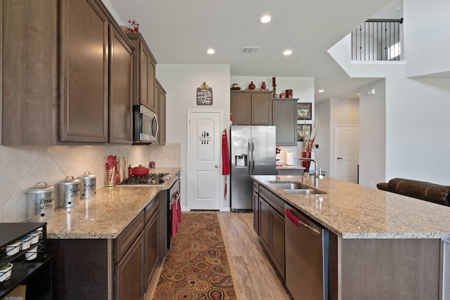 25718 Balsamwood Dr, Tomball, TX 77375 - kitchen featuring appliances with stainless steel finishes, wood finished floors, an island with sink, backsplash, and light stone counters