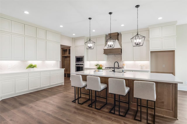 1437 Bluebonnet Ridge Dr, Chappell Hill, TX 77426 - kitchen with appliances with stainless steel finishes, custom exhaust hood, tasteful backsplash, a center island with sink, and light countertops