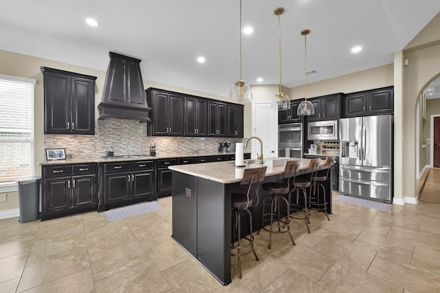 116 Owen Ridge Dr, Conroe, TX 77384 - kitchen with stainless steel appliances, custom exhaust hood, dark cabinetry, backsplash, and a kitchen bar
