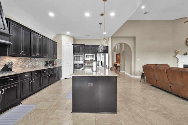 116 Owen Ridge Dr, Conroe, TX 77384 - kitchen featuring arched walkways, appliances with stainless steel finishes, dark cabinets, open floor plan, and tasteful backsplash