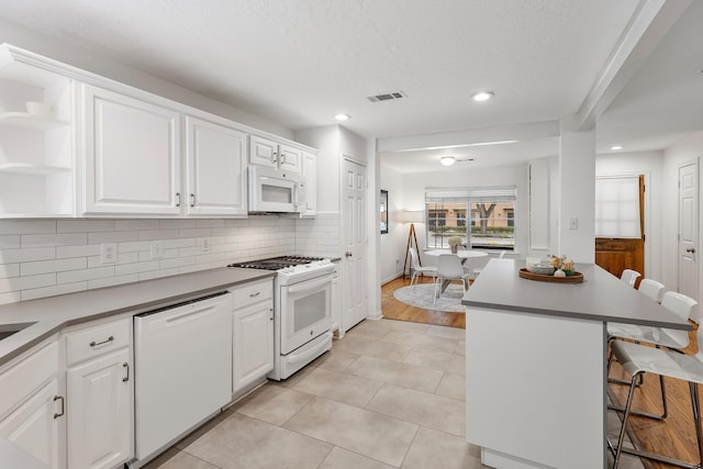 3923 W Main St, Houston, TX 77027 - kitchen featuring white appliances, a breakfast bar area, backsplash, open shelves, and white cabinets