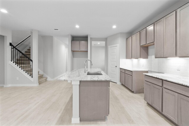 2547 Forest Cedar Ln, Conroe, TX 77301 - kitchen with light stone countertops, a kitchen island with sink, light wood-style floors, recessed lighting, and decorative backsplash