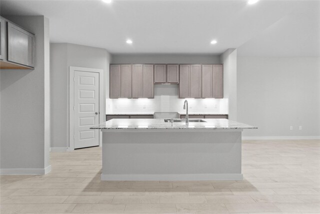 2547 Forest Cedar Ln, Conroe, TX 77301 - kitchen with decorative backsplash, a center island with sink, recessed lighting, light stone counters, and light wood finished floors
