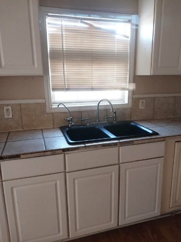 1311 Lamar Ave, Big Spring, TX 79720 - kitchen with a sink, white cabinets, decorative backsplash, and tile counters