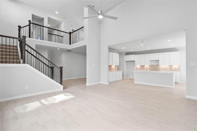 2008 Sugarberry Gully Ln, Conroe, TX 77301 - unfurnished living room with light wood-type flooring, a ceiling fan, stairway, a high ceiling, and baseboards