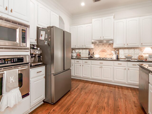 4133 Dickson St, Houston, TX 77007 - kitchen featuring appliances with stainless steel finishes, under cabinet range hood, ornamental molding, dark countertops, and white cabinetry