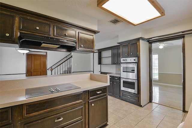 5411 Mossy Timbers Dr, Humble, TX 77346 - kitchen with stainless steel double oven, black electric stovetop, under cabinet range hood, light tile patterned floors, and dark brown cabinetry
