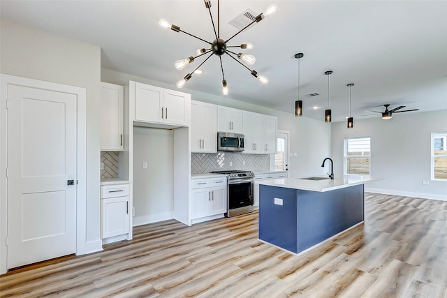5407 Lee St, Houston, TX 77020 - kitchen featuring appliances with stainless steel finishes, white cabinetry, decorative backsplash, light wood-type flooring, and a chandelier