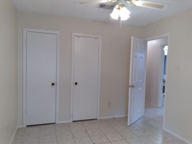2450 Edgedale Dr, Missouri City, TX 77489 - unfurnished bedroom with light tile patterned floors, ceiling fan, and two closets