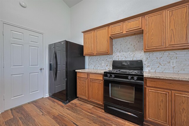 19826 Imperial Stone Dr, Houston, TX 77073 - kitchen with black appliances, decorative backsplash, brown cabinetry, dark wood-type flooring, and light stone counters