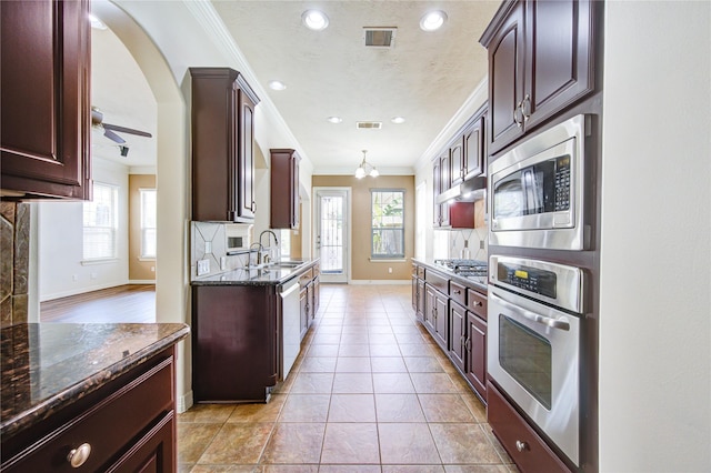 14410 Basalt Ln, Houston, TX 77077 - kitchen featuring appliances with stainless steel finishes, ornamental molding, baseboards, dark stone countertops, and dark brown cabinetry