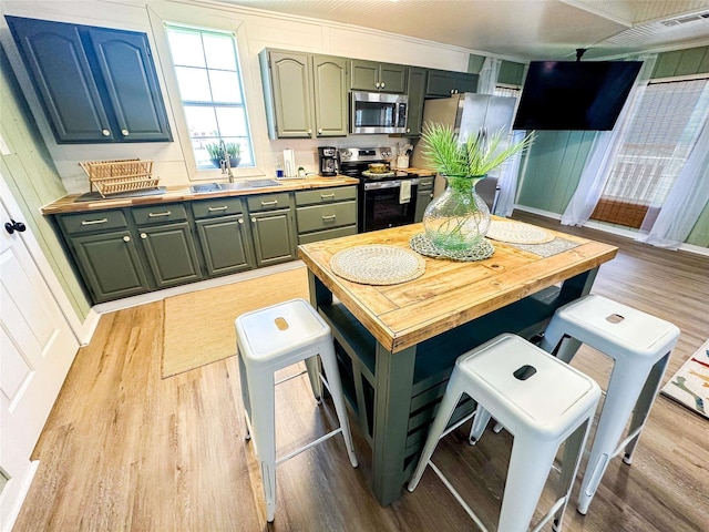 1032 N Selwyn Rd, Crystal Beach, TX 77650 - kitchen with stainless steel appliances, light wood finished floors, butcher block countertops, a breakfast bar, and green cabinetry