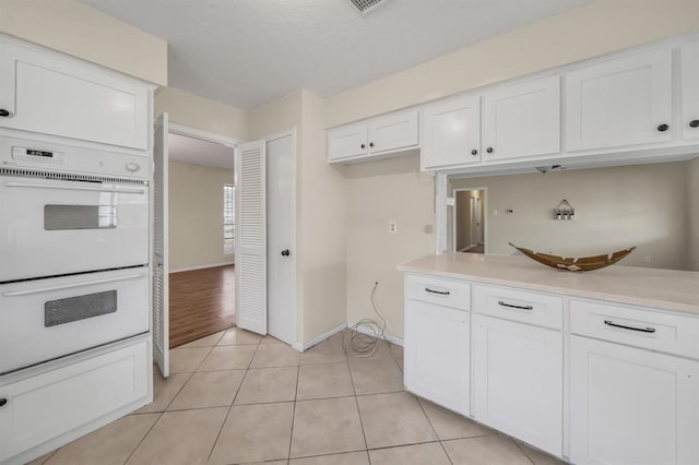 9039 Sandstone St, Houston, TX 77036 - kitchen featuring white double oven, white cabinetry, light countertops, baseboards, and light tile patterned floors
