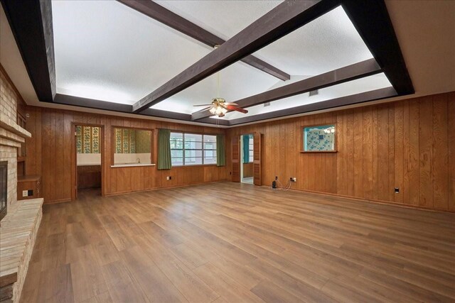 5210 Linda Ln, Beaumont, TX 77708 - unfurnished living room with a brick fireplace, ceiling fan, beam ceiling, wooden walls, and wood finished floors