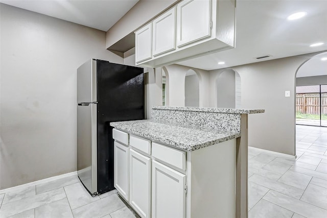 22910 Summer Green Ln, Spring, TX 77373 - kitchen featuring freestanding refrigerator, arched walkways, white cabinets, light stone counters, and recessed lighting